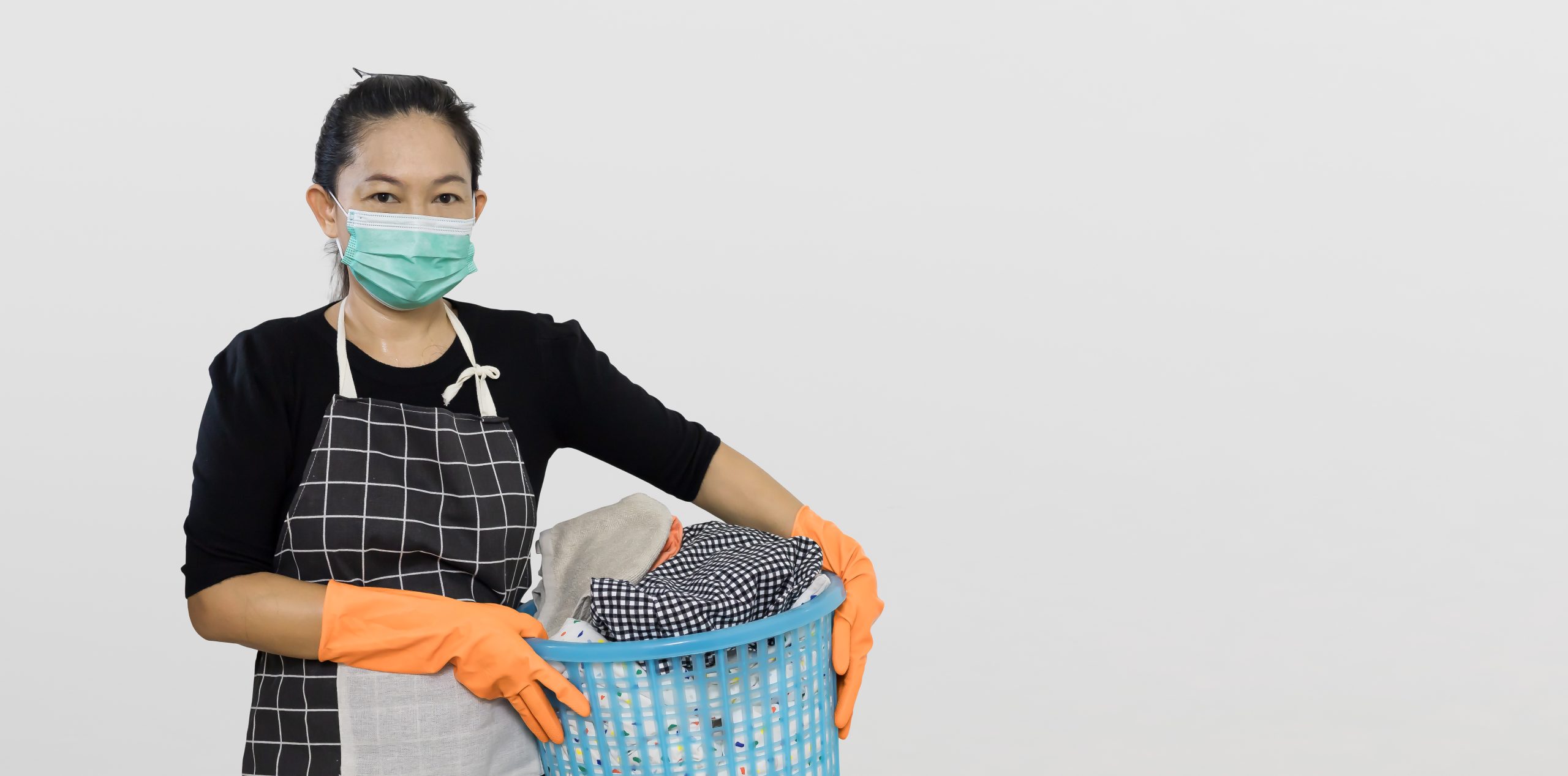 Maid in apron and gloves carrying laundry, representing the household work behind a fair salary in Singapore.